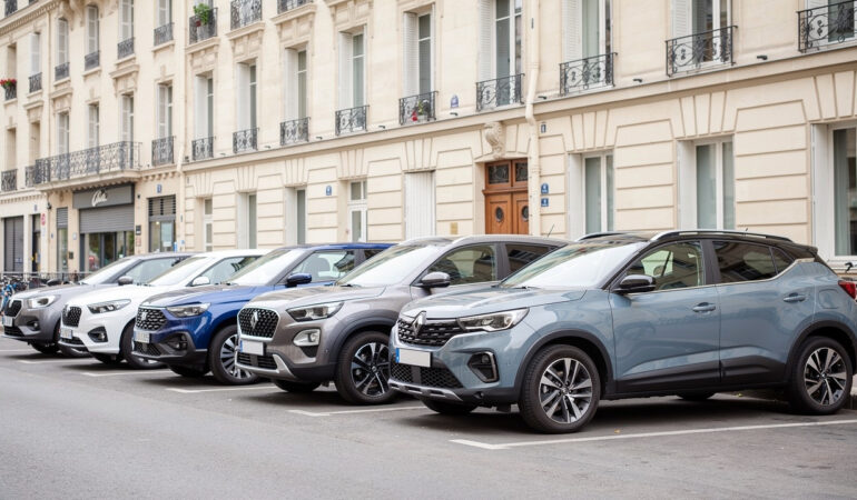 Plusieurs SUV compacts récents de tailles différentes sont stationnés en ligne dans une rue urbaine française éclairée par une lumière naturelle.